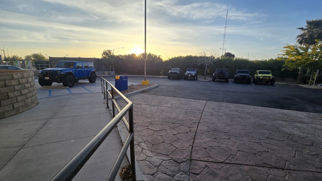 Dusk view of a parking lot featuring several off-road vehicles parked together, staged and prepped for a desert expedition.